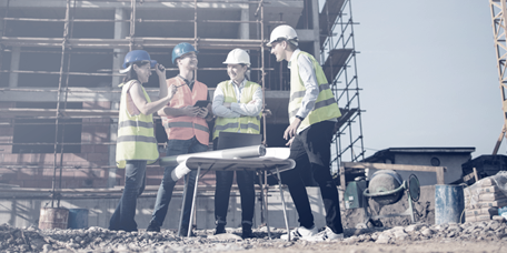 Operai raggruppati intorno a piani di costruzione davanti a un edificio in costruzione